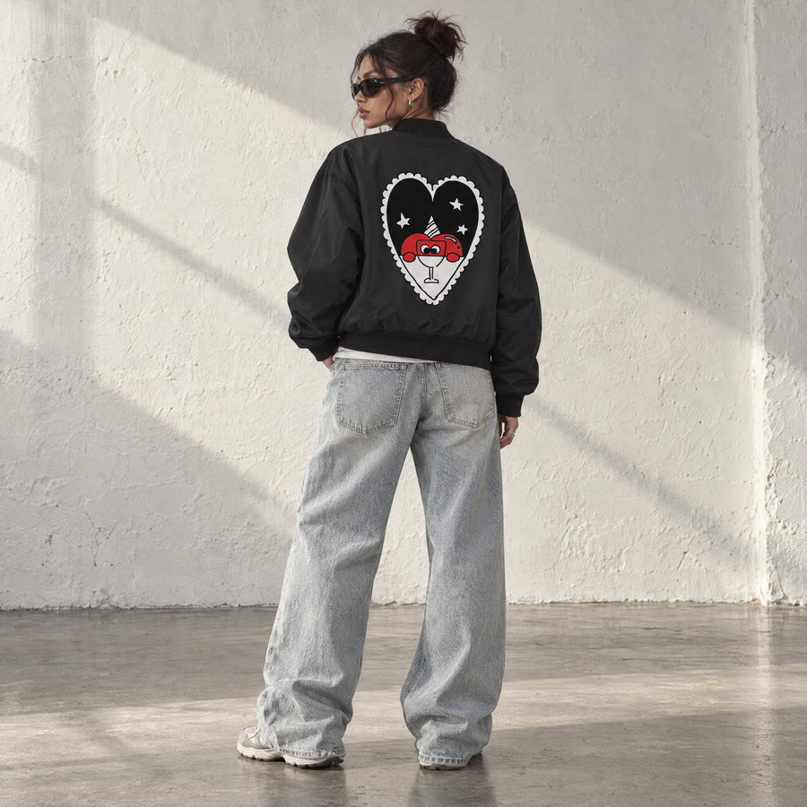 Model wearing the Appuri Heart College Bomber, back view showing the back print, in a sunlit studio